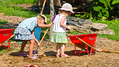 Two girls dig in the dirt in an outdoor classroom